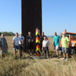 Gruppe von Männern neben einer kleinen schwarz-rot-gelben Grenzsäule